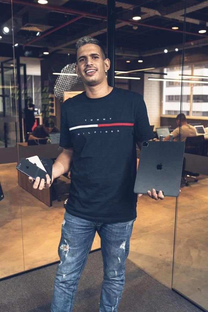 Tyago Sena em um escritório segurando iPhones e um iPad