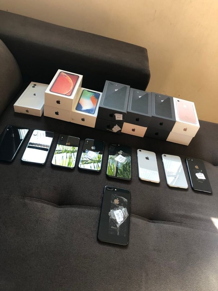 Lote de iPhones e caixas organizados sobre um sofá, com etiquetas de memória e bateria